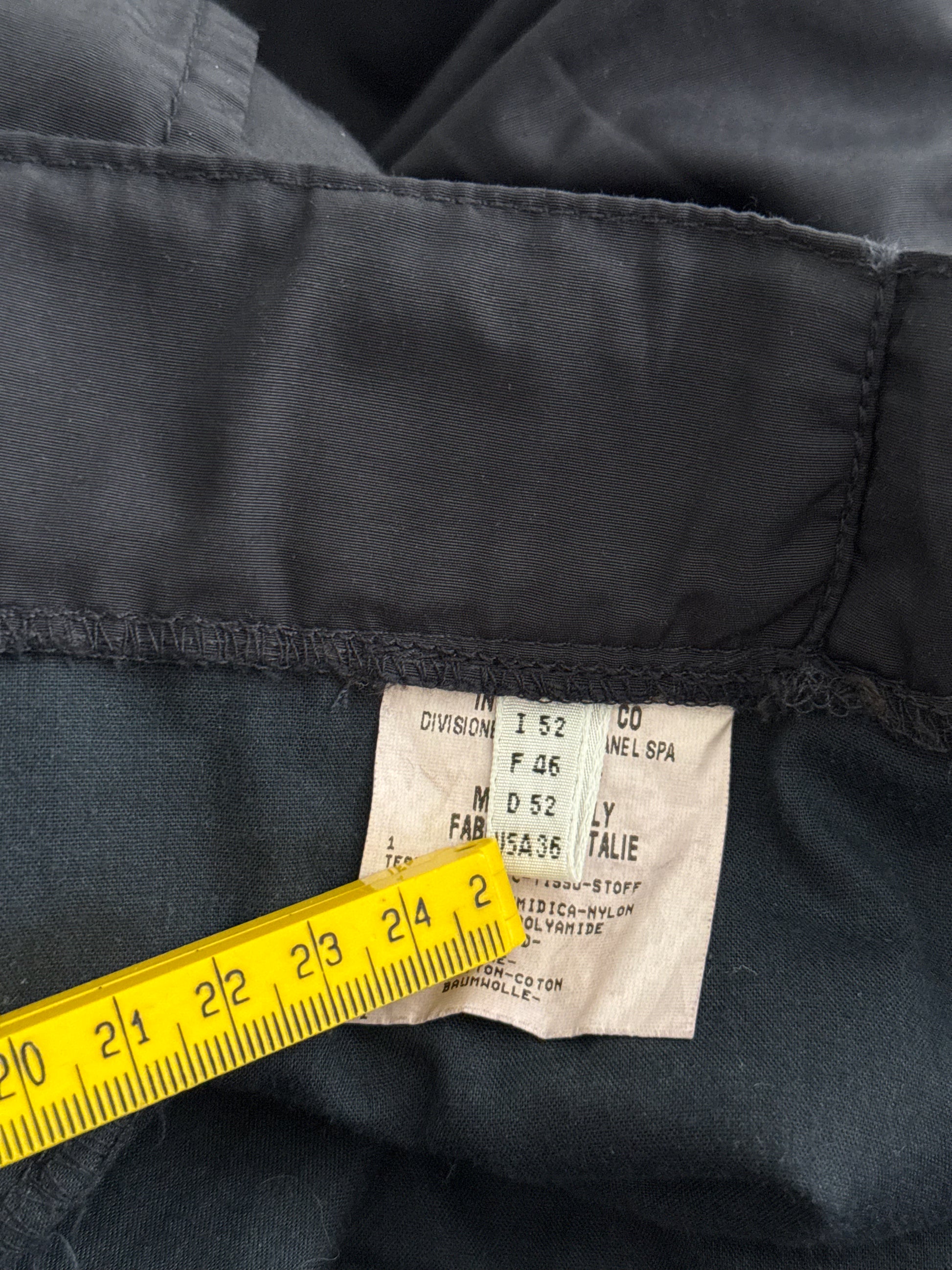 Close-up of a black fabric garment with a label and yellow measuring tape.