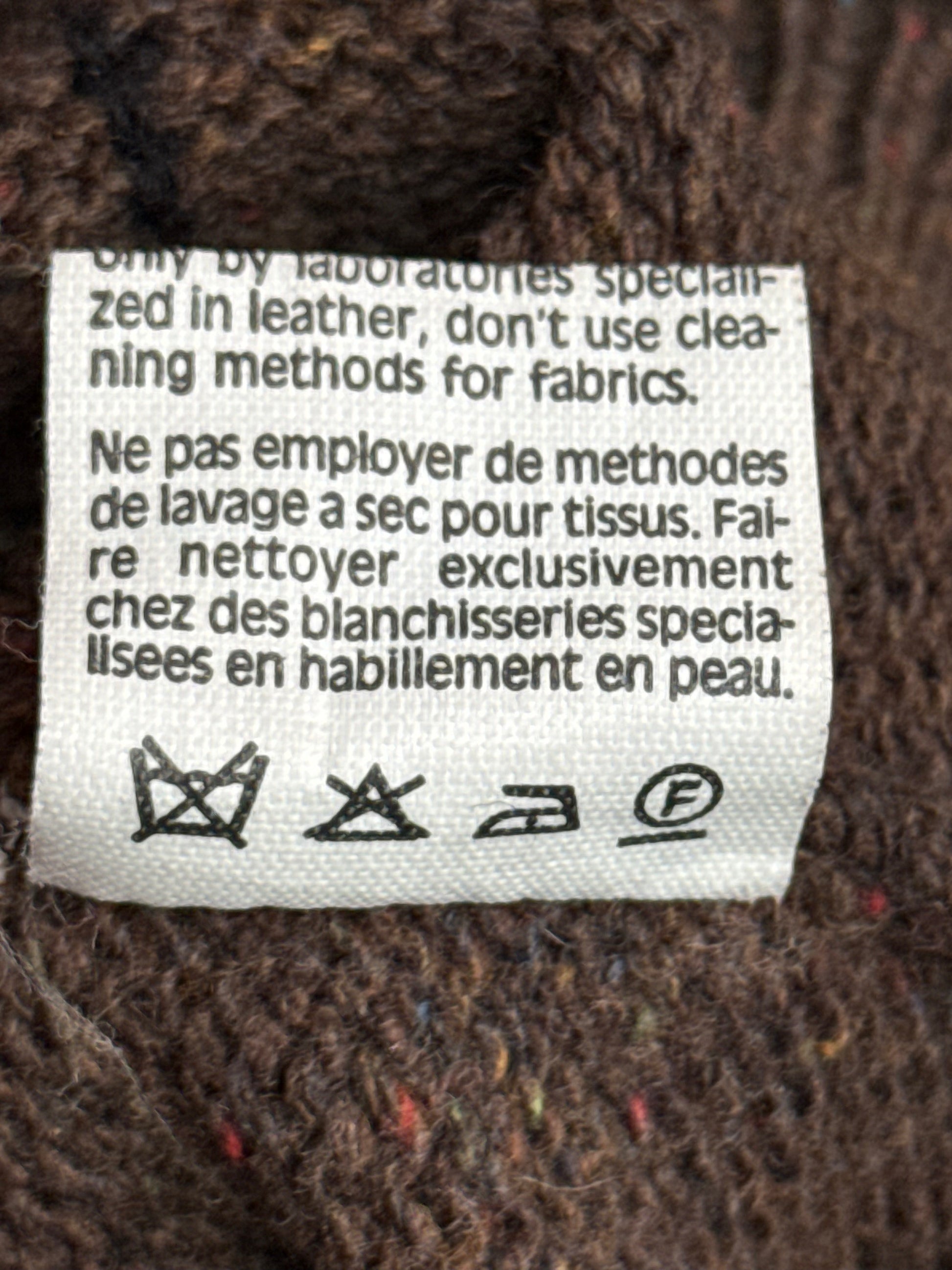 Clothing label on a textured fabric background with care instructions.