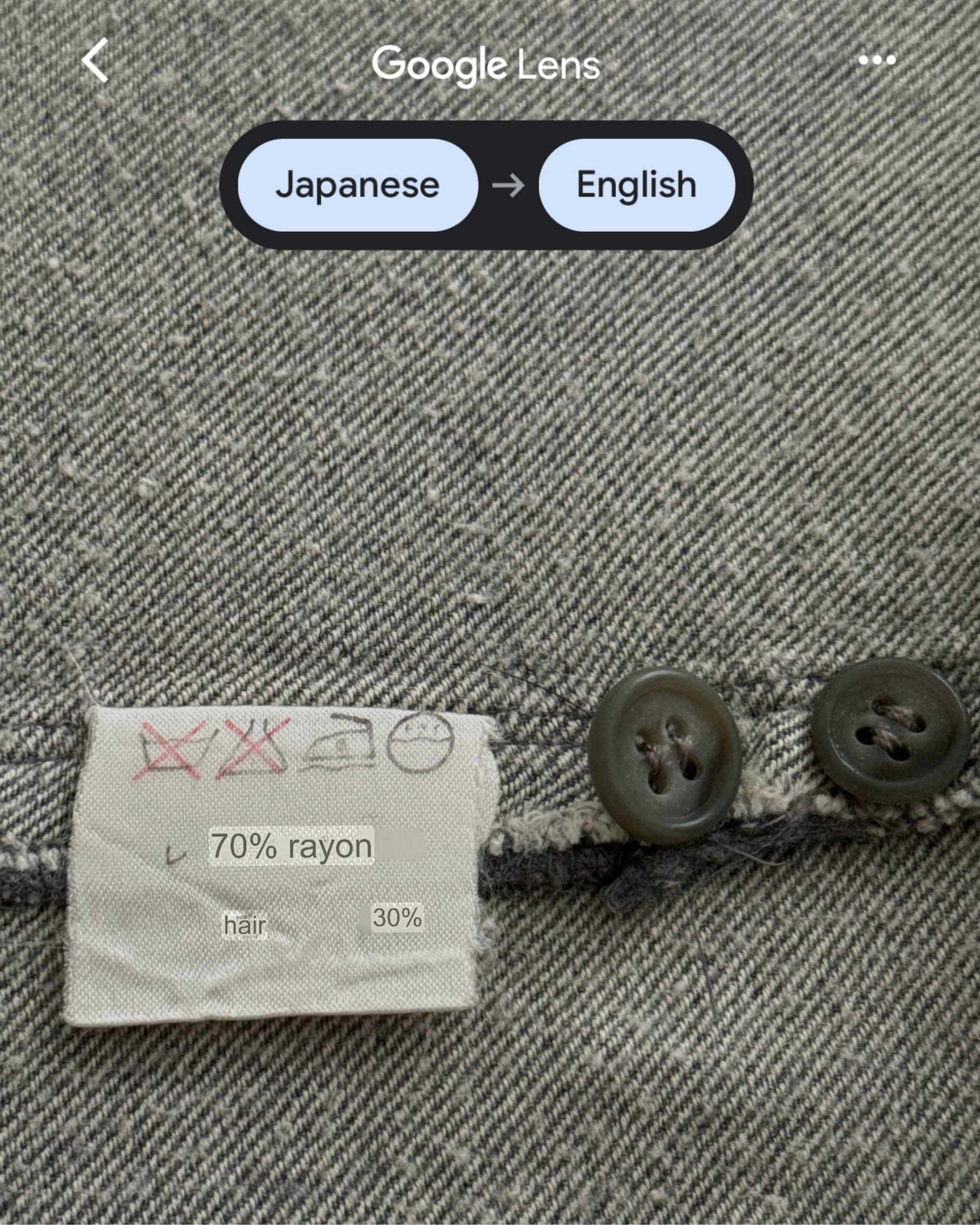 Textile label on a gray fabric with buttons, featuring text in Japanese and English.